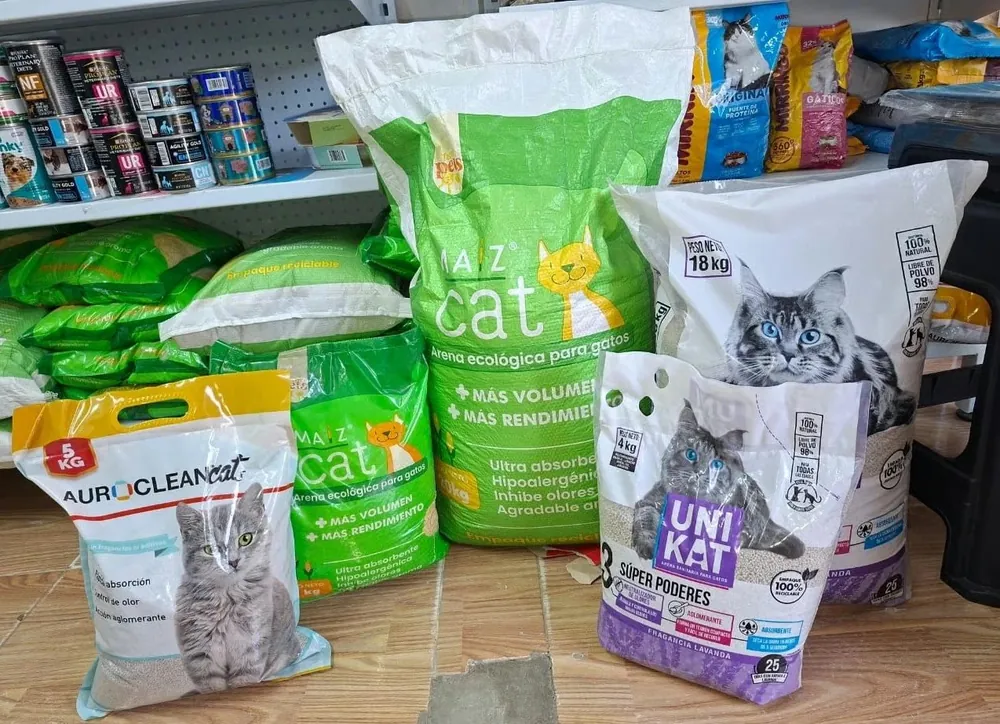 Bultos de arena para gatos exhibidos en Patitas Pet Shop: Auroclean Cat, Máz Cat y Unikat con fragancia lavanda, y al fondo latas de comida para gatos