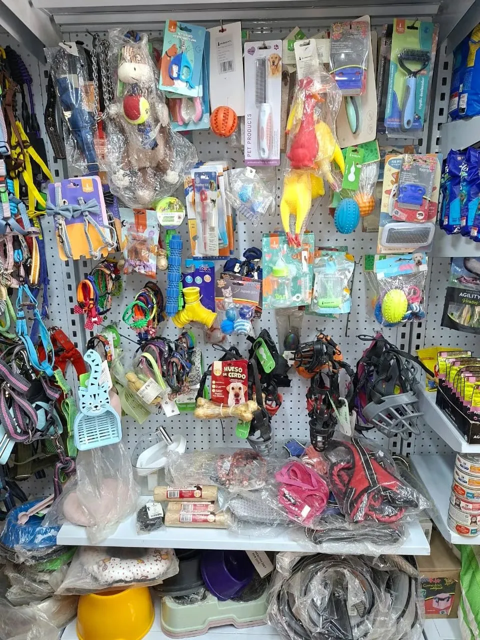 Exhibidor de accesorios y juguetes en Patitas Pet Shop: correas y arneses de colores, pelotas, peluches, huesos, cepillos, cortaúñas y juguetes de cuerda para perros y gatos