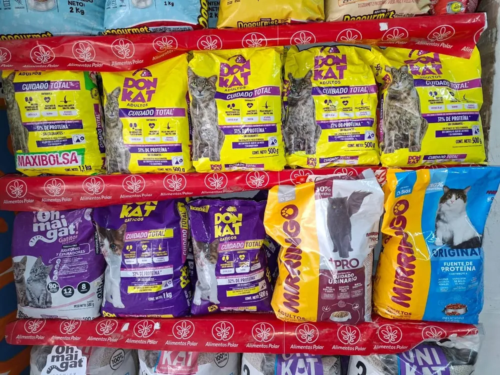Colección de bultos de comida para gatos exhibidos en estanterías rojas, con bolsas amarillas Maxi Bolsa y paquetes morados y multicolores de Don Kat, Kat y Mirringo